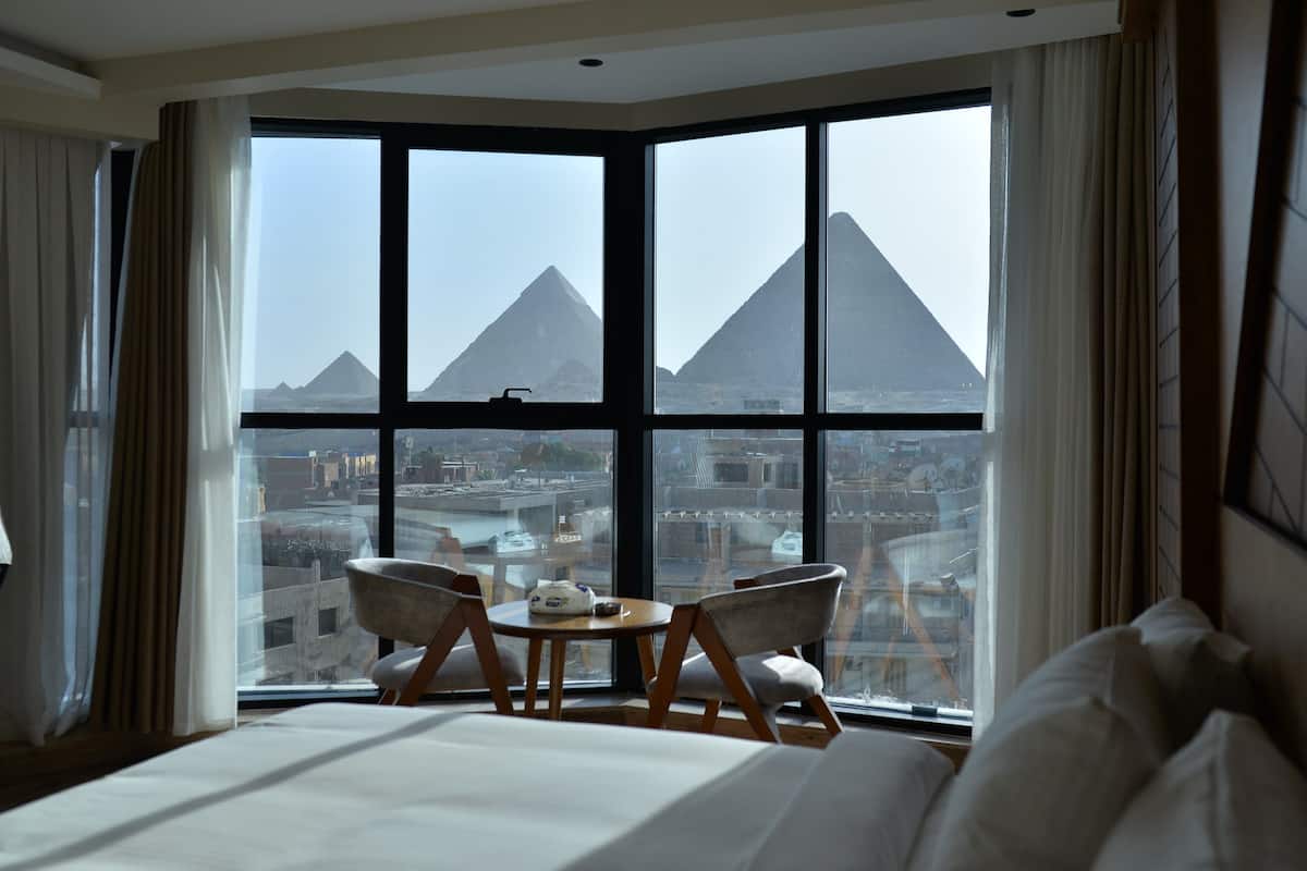 A hotel room with a large window offering a view of pyramids.