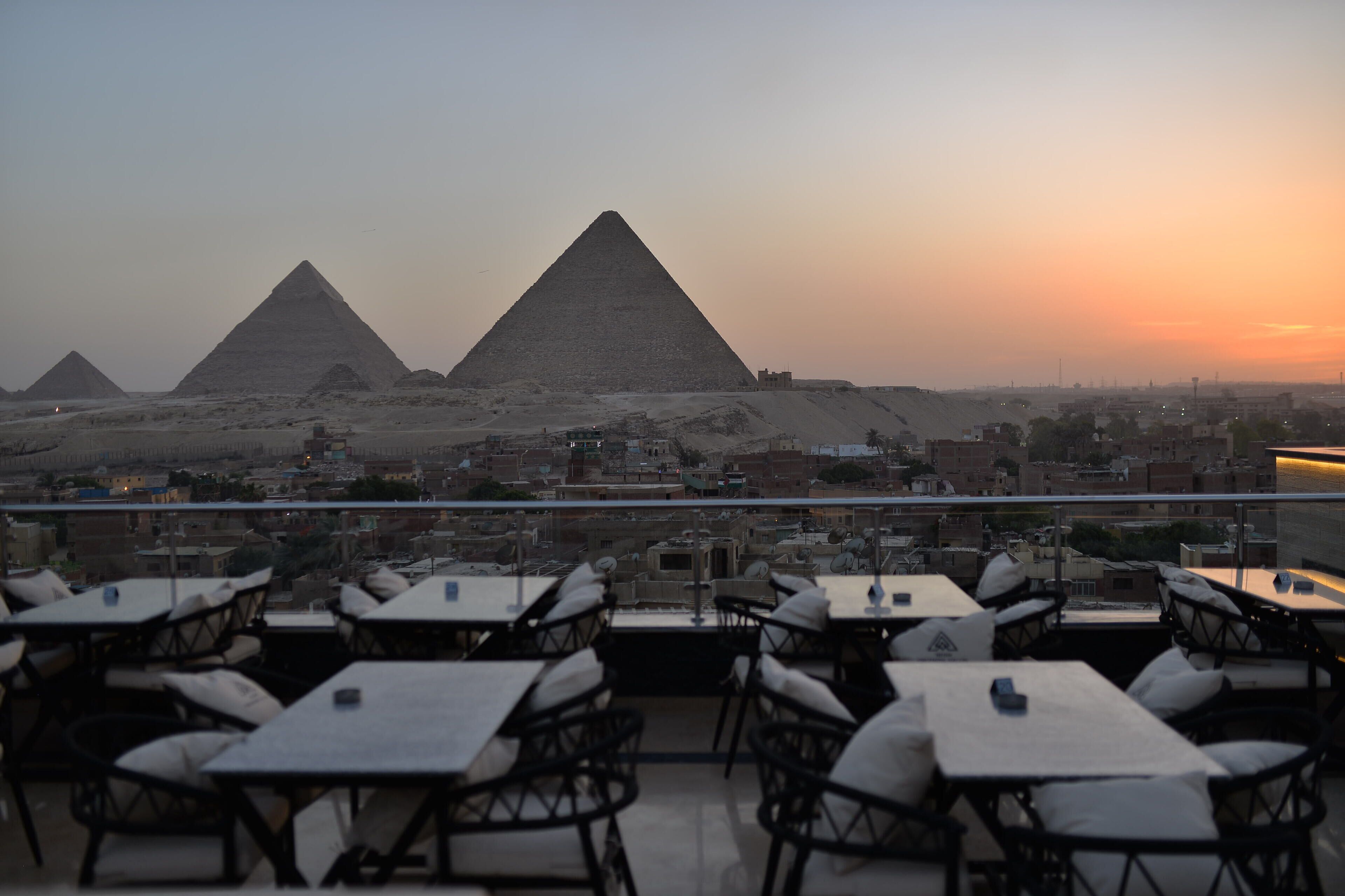 Eine Dachterrasse mit Tischen und Stühlen mit Blick auf die Pyramiden bei Sonnenuntergang.