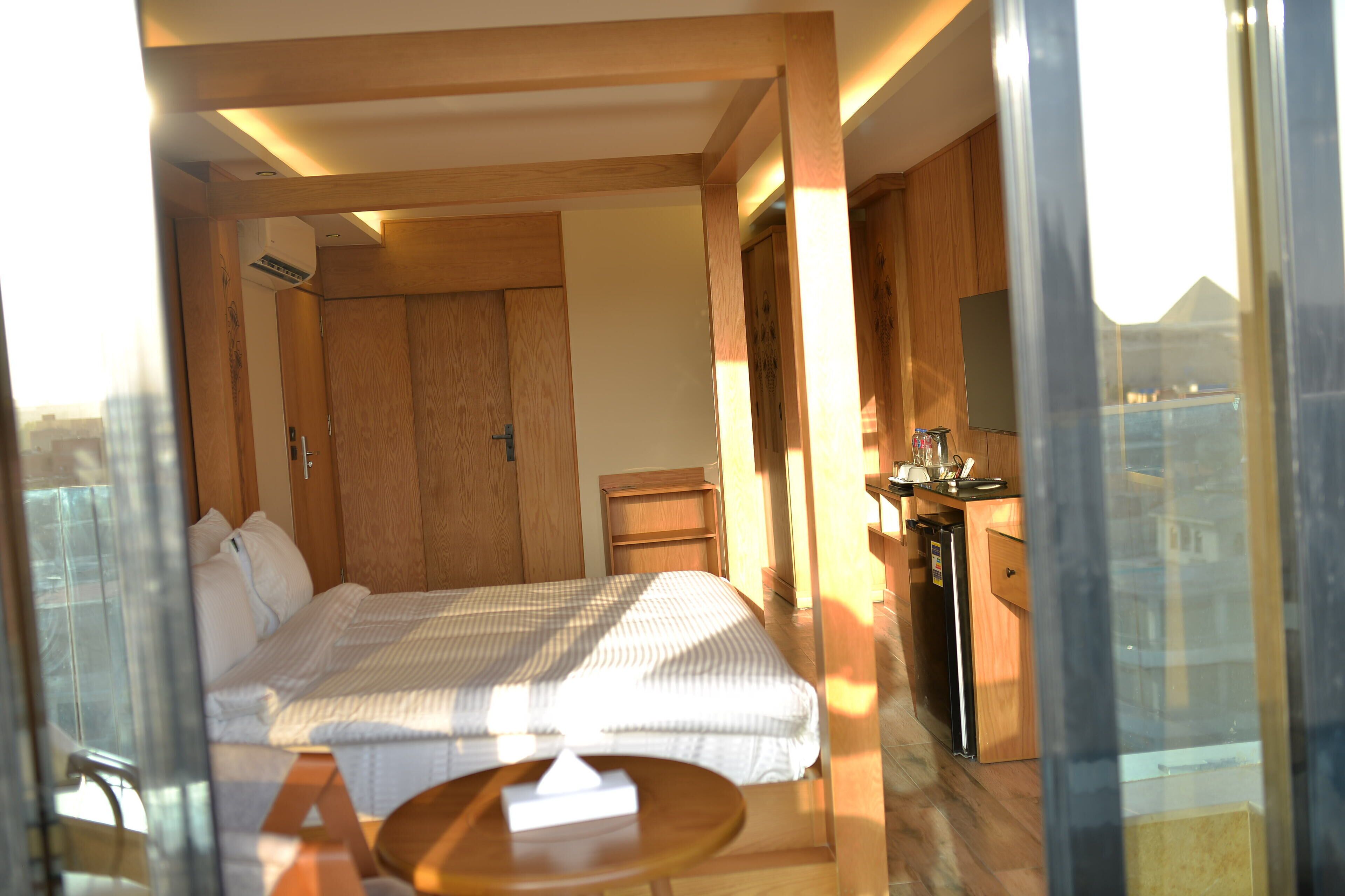 A hotel room with a bed, bedside table, and a small kitchenette area.