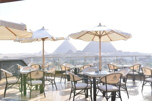 A rooftop terrace with tables and chairs, umbrellas, and a view of mountains.