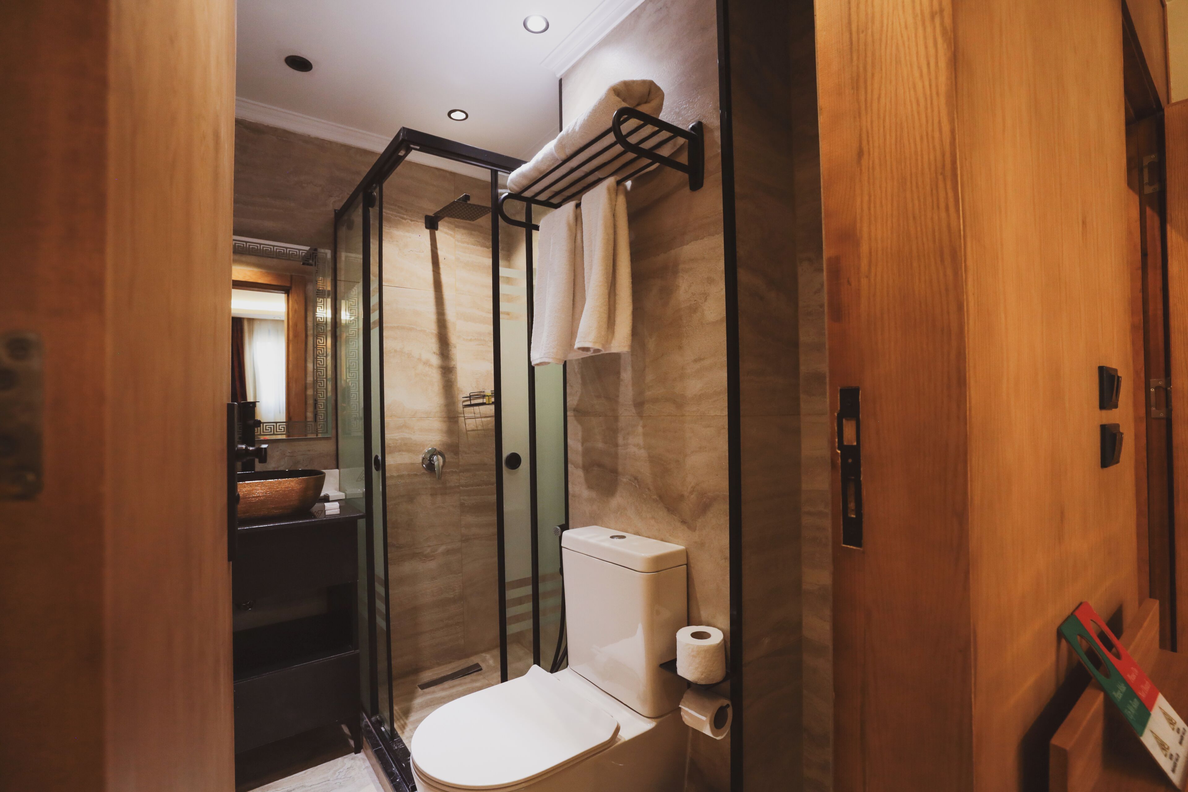 A modern bathroom with a glass-enclosed shower, a wooden vanity, and a toilet with a towel rack above it.