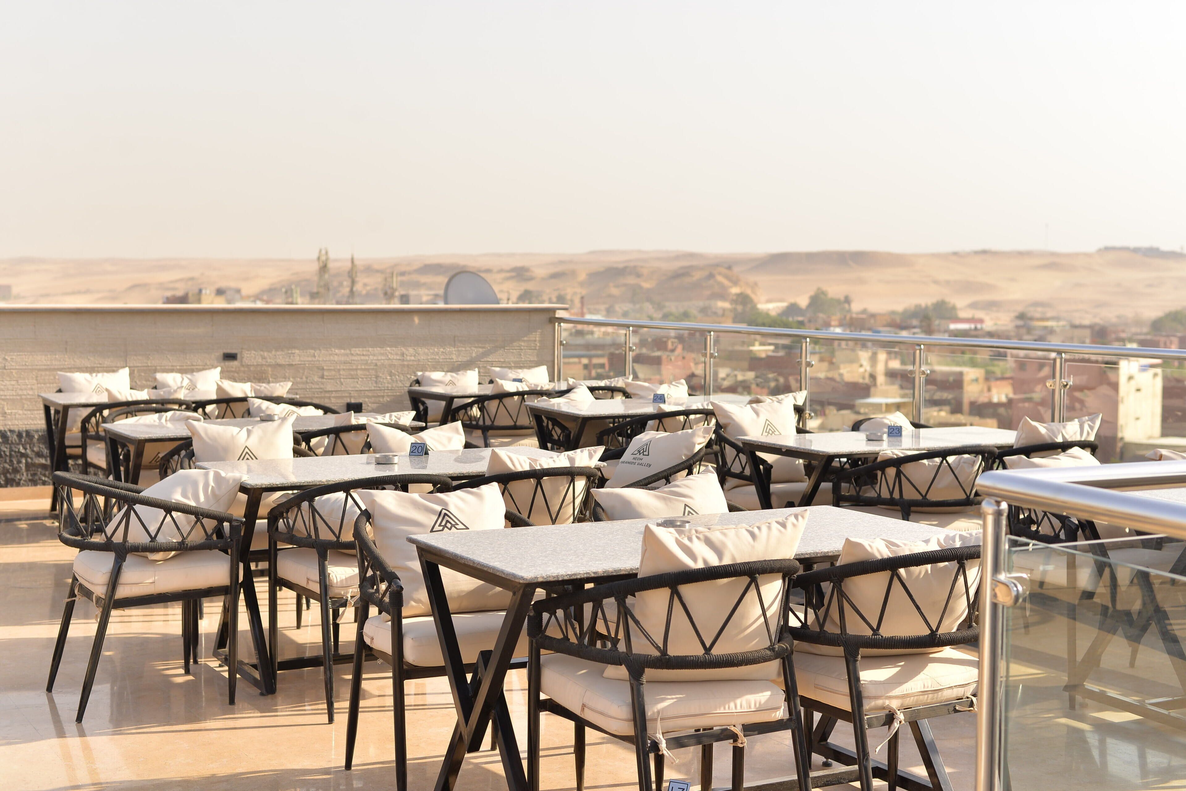 Outdoor seating with tables and chairs, a glass railing, and a view of a distant landscape.