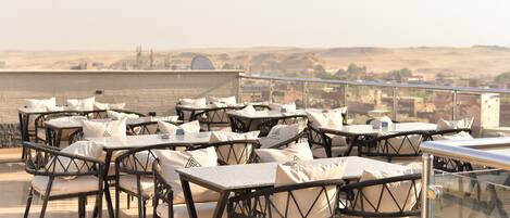 Outdoor seating with tables and chairs, a glass railing, and a view of a distant landscape.