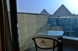 A balcony with a glass table and chairs, a view of the pyramids, and a wall with a textured pattern.