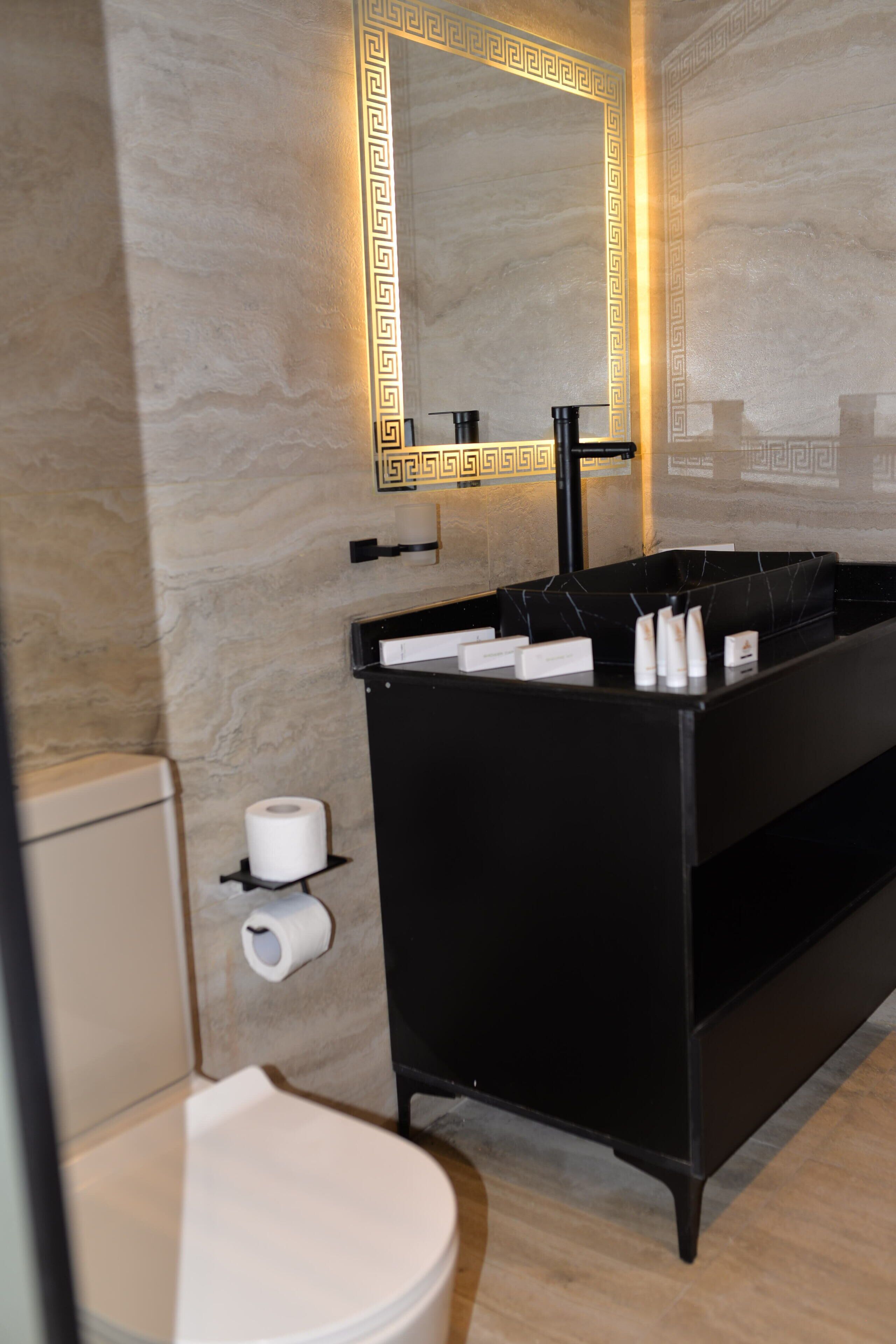 Et moderne badeværelse med en sort kommode, toilet og et spejl med dekorativ ramme.