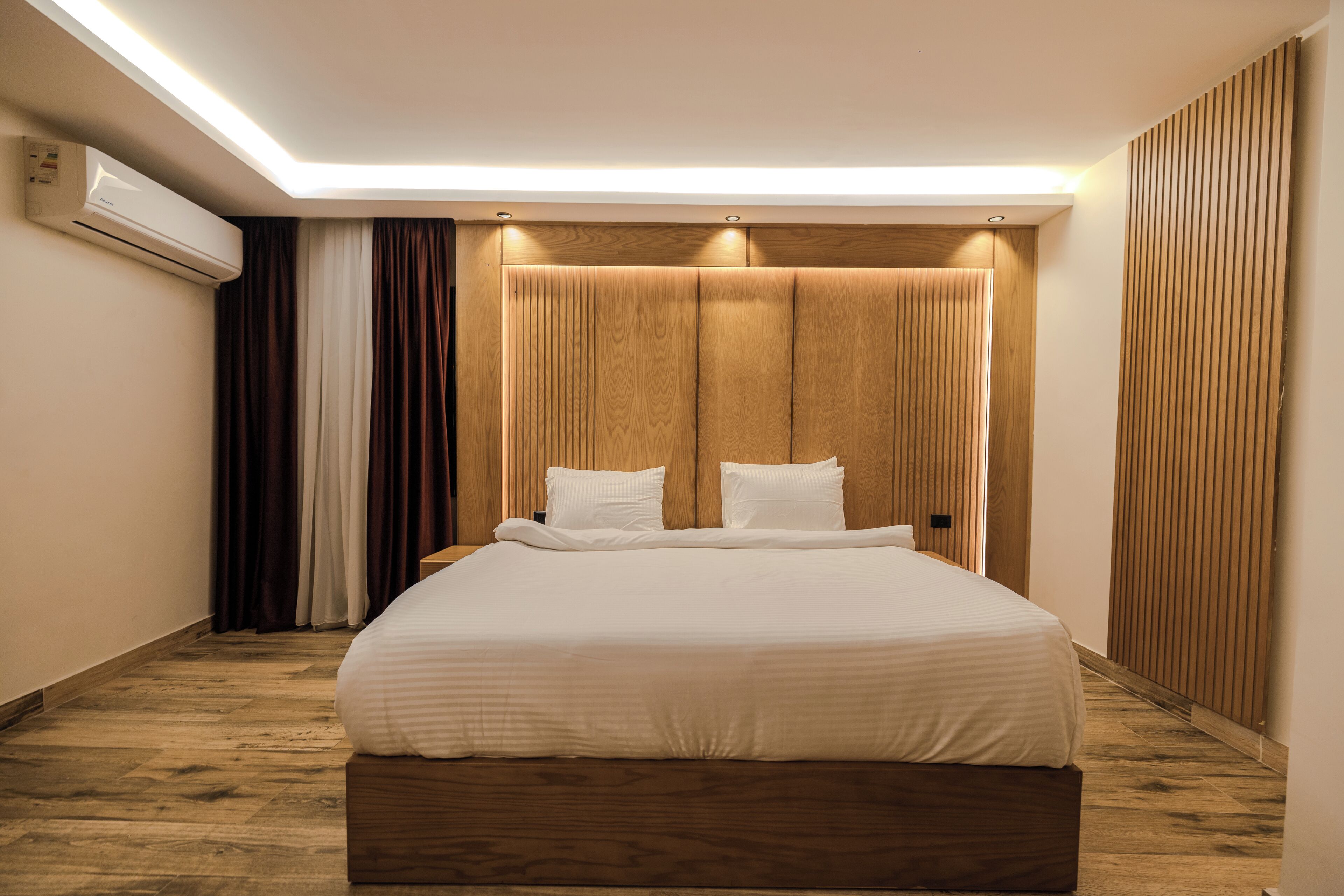 Una camera d'albergo moderna con un grande letto, pannelli di legno sulle pareti e un condizionatore d'aria a parete.