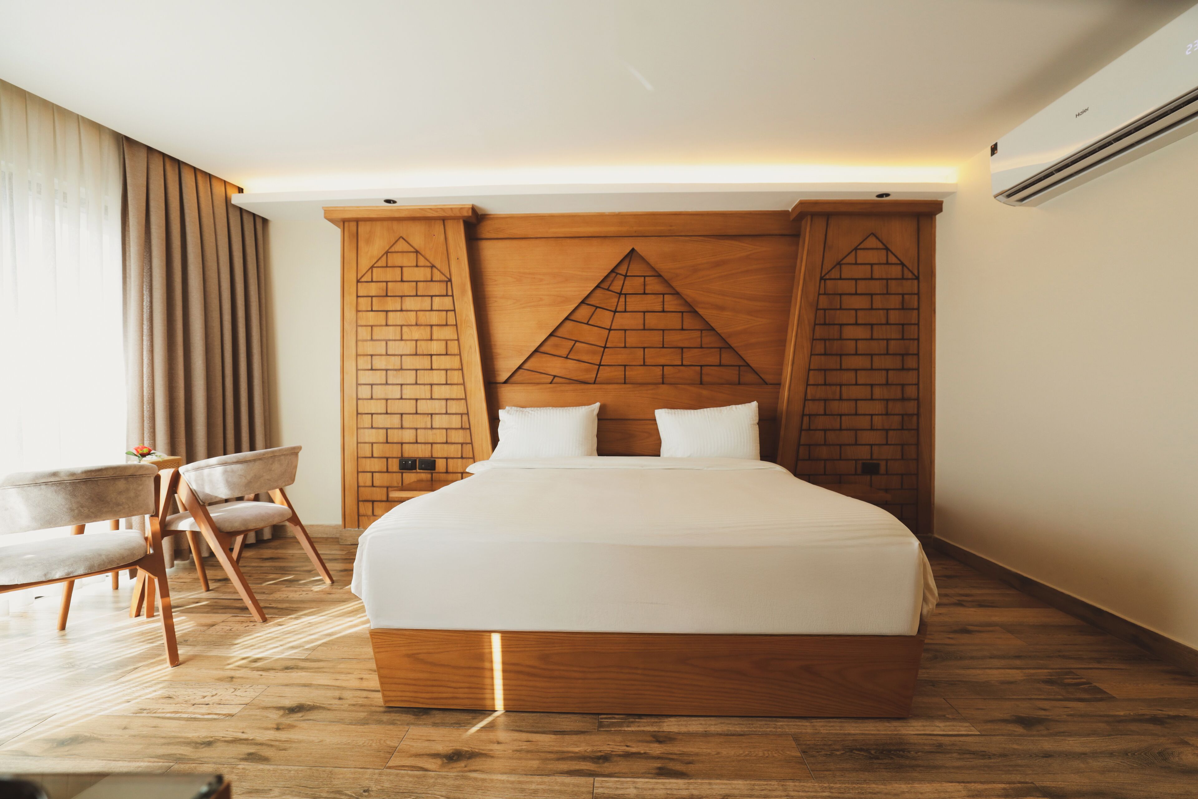 A modern hotel room with a large bed, wooden headboard, and a seating area with chairs.