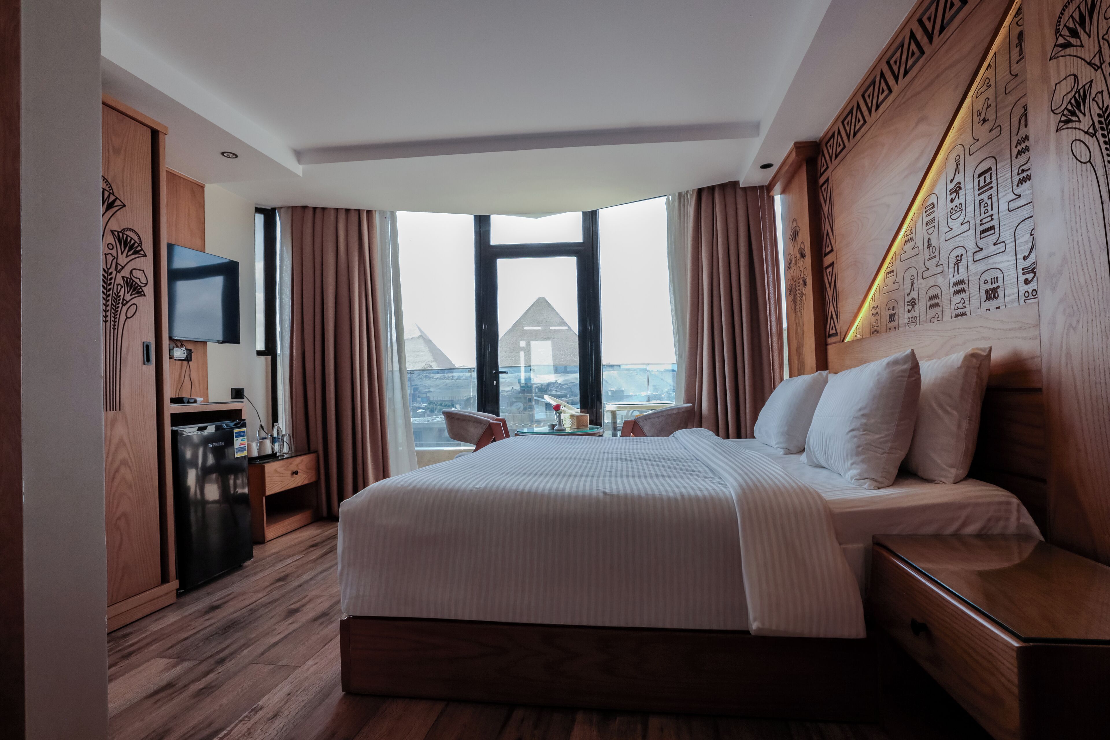 Une chambre d’hôtel avec un grand lit, un bureau, une télévision et une vue sur le paysage urbain, grâce à de grandes fenêtres.