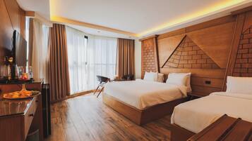 A hotel room with two beds, a wooden headboard, a flat-screen TV, a desk with a coffee maker, and a dining table with a plate of food.