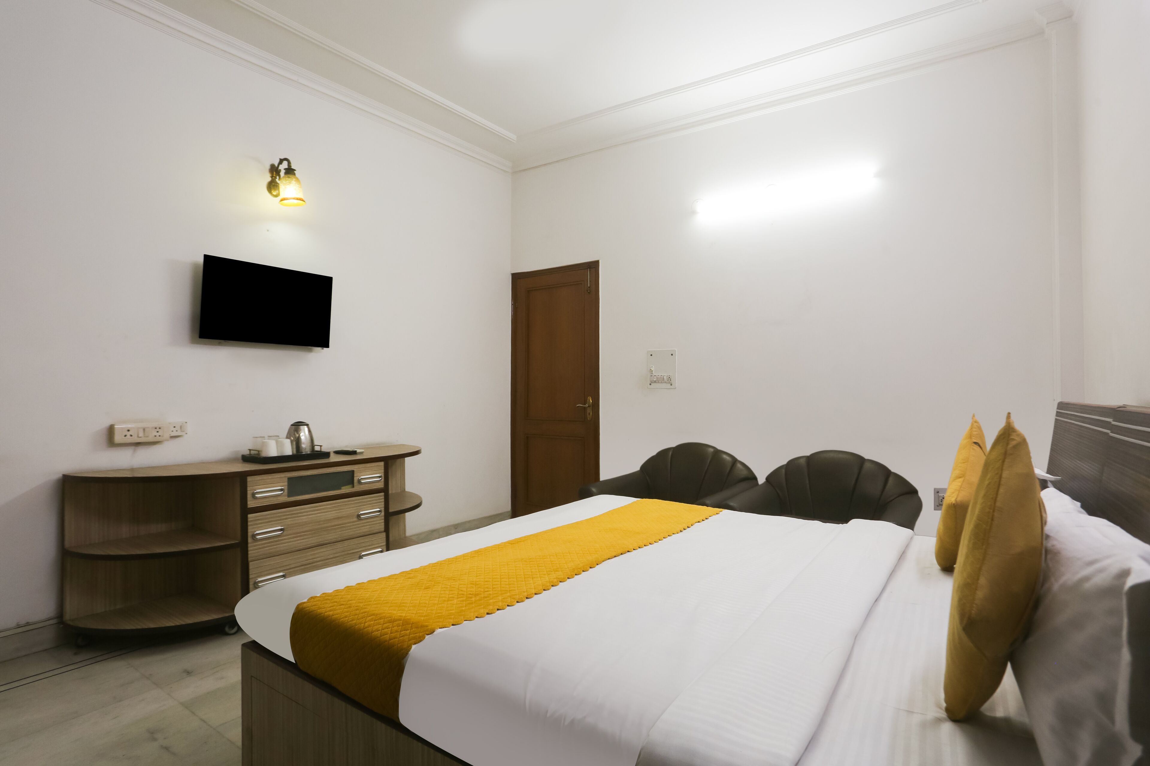 Una habitación de hotel con una cama, un televisor montado en la pared, un aparador de madera y una puerta.