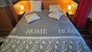 Ein ordentlich bezogenes Bett mit einem blumigem Bettbezug und Kissen, zwei Nachttische mit Lampen sowie ein Kopfteil mit Holzvertäfelung.