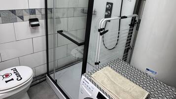 A bathroom with a glass-enclosed shower, a toilet, and a front-loading washing machine.
