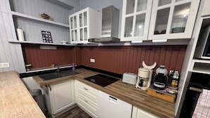 Eine kleine Küche mit weißen Schränken, einer Holz Arbeitsplatte, einem eingebauten Geschirrspüler und einer Kaffeemaschine.