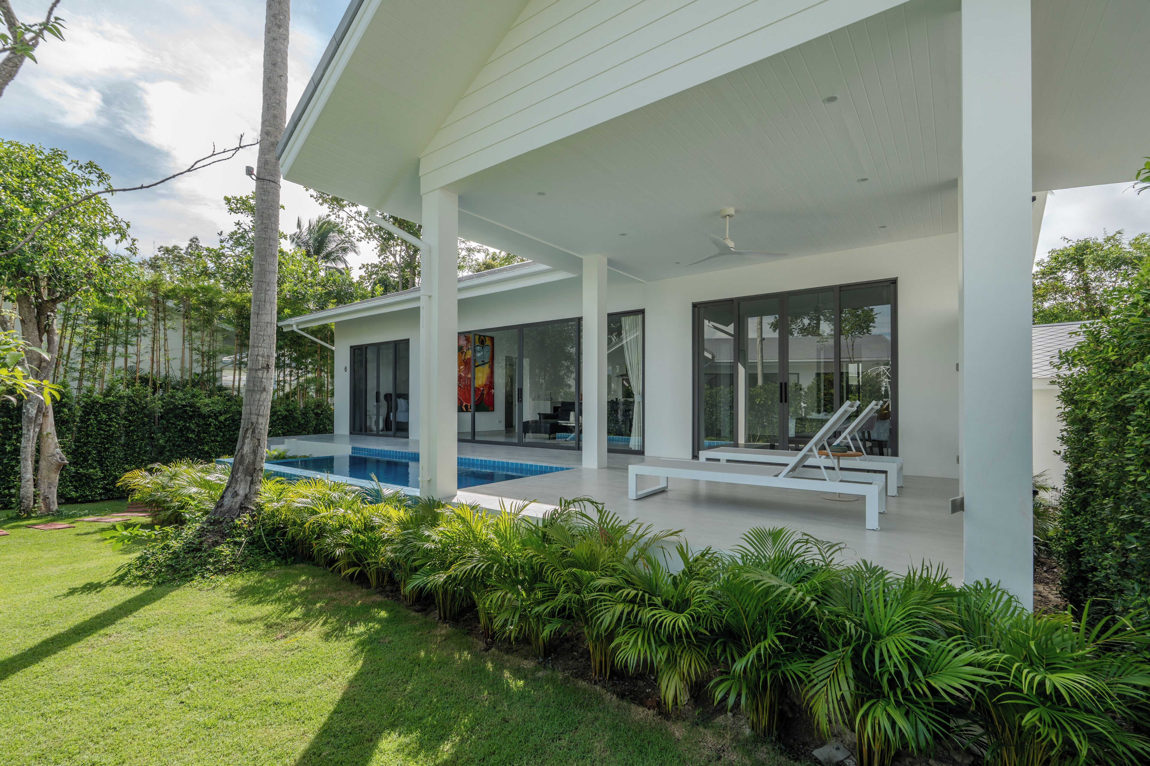 A modern house with a covered patio, a swimming pool, and lush greenery.