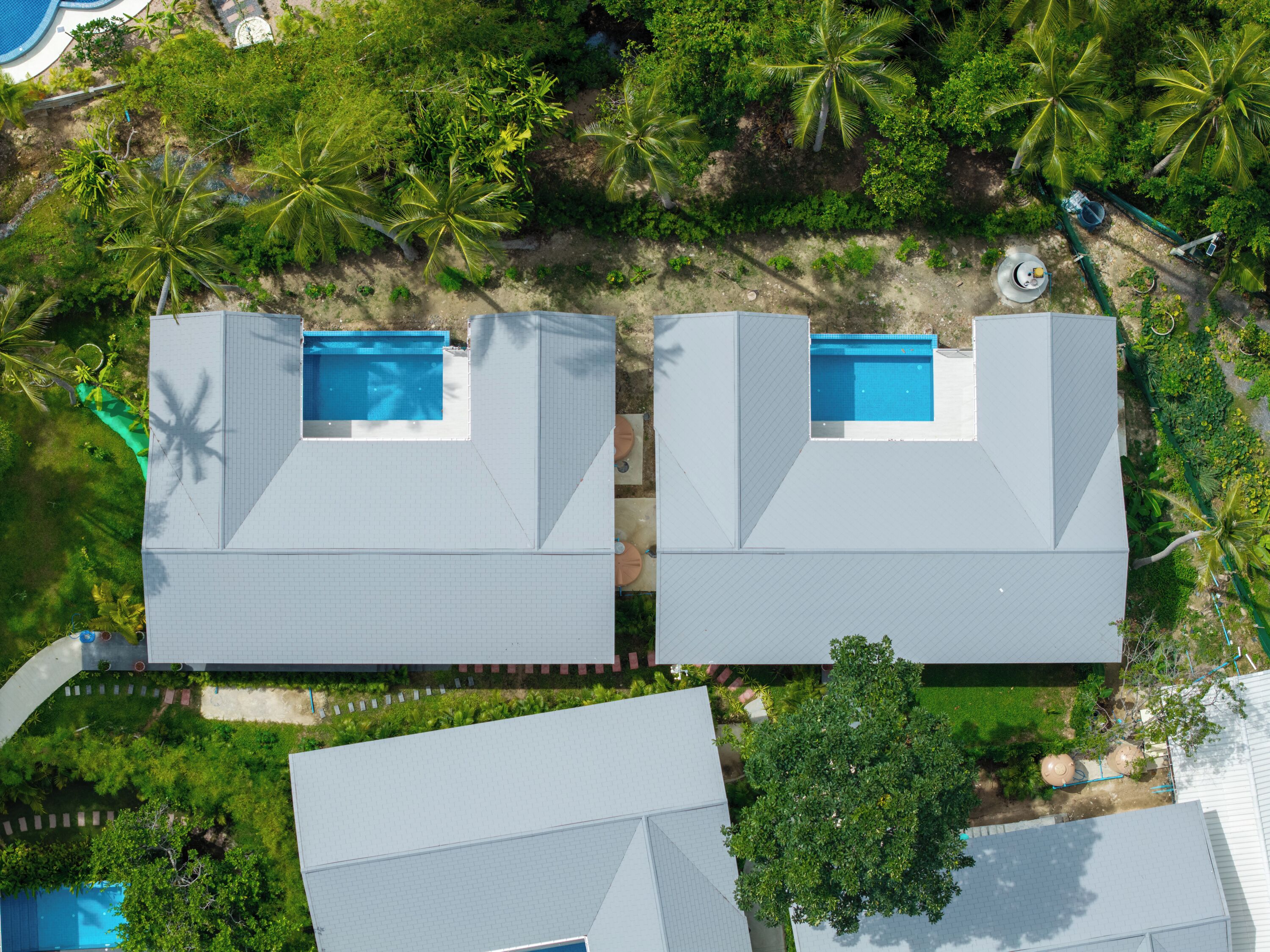 Un quartier résidentiel comprenant deux maisons, chacune dotée d’une piscine, et entouré d’une végétation luxuriante et de palmiers.