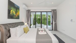 A modern hotel room with a large bed, a view of greenery through the sliding glass doors, and a ceiling fan.