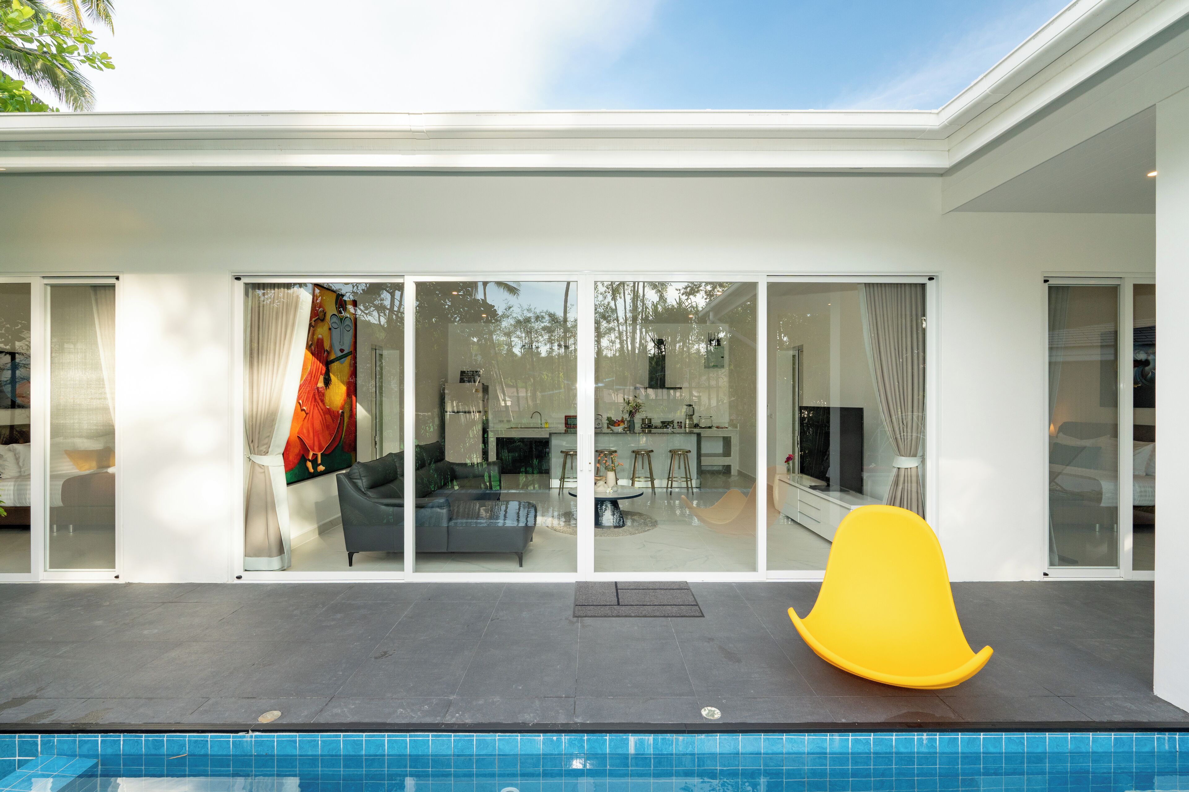 Una casa moderna con piscina, puertas correderas de vidrio grandes y una silla amarilla brillante junto a la piscina.