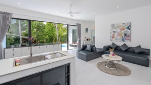A modern living room with a grey sofa, a round coffee table, and a large window overlooking a garden.