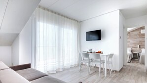 Una sala de estar moderna con un sofá, un comedor con sillas, un televisor montado en la pared y una escalera que conduce a otra habitación.