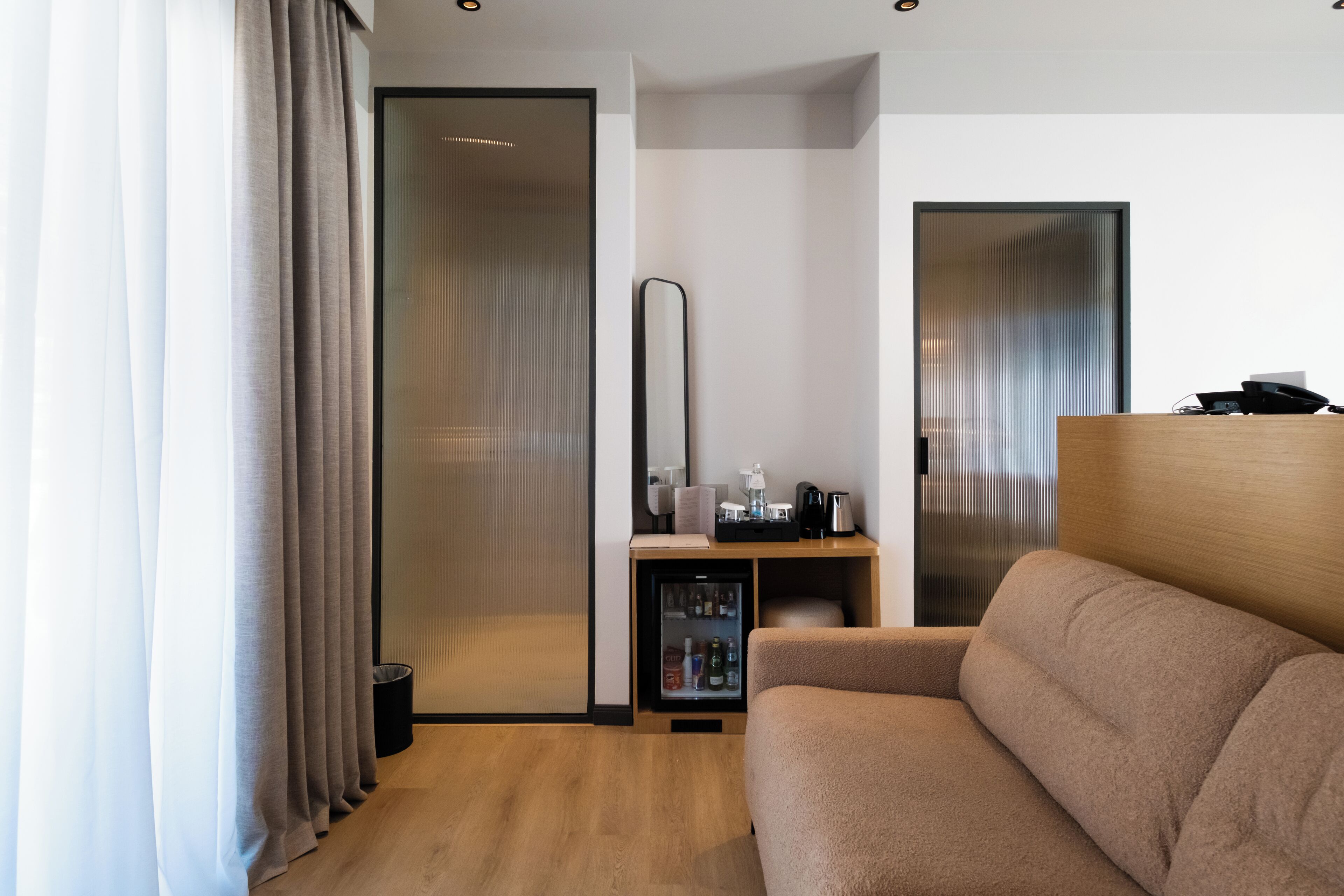 Une chambre d’hôtel moderne avec un plancher en bois, un canapé beige, un minibar et une porte coulissante.