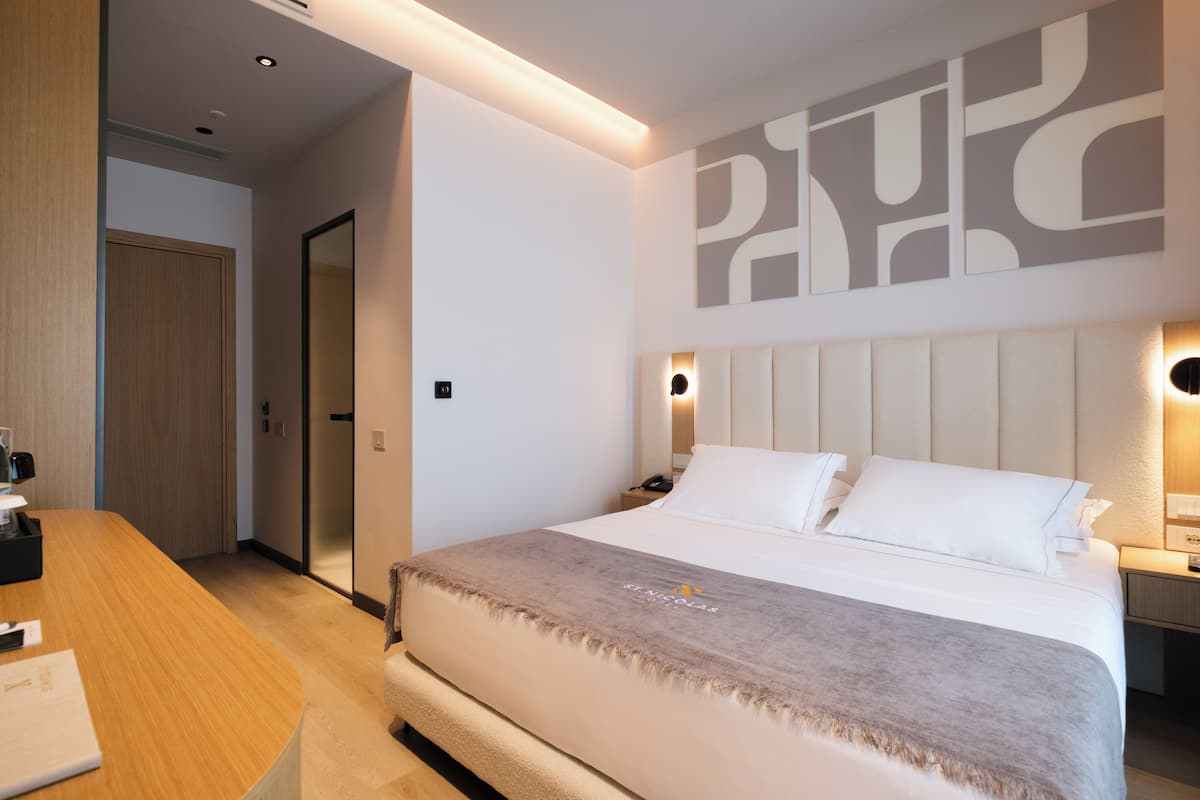 A modern hotel room with a large bed, a wooden desk, and a wall-mounted artwork.