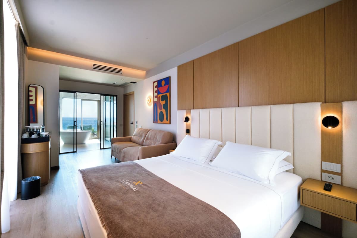 A hotel room with a large bed, a sofa, a desk with a computer, and a view of the outside.