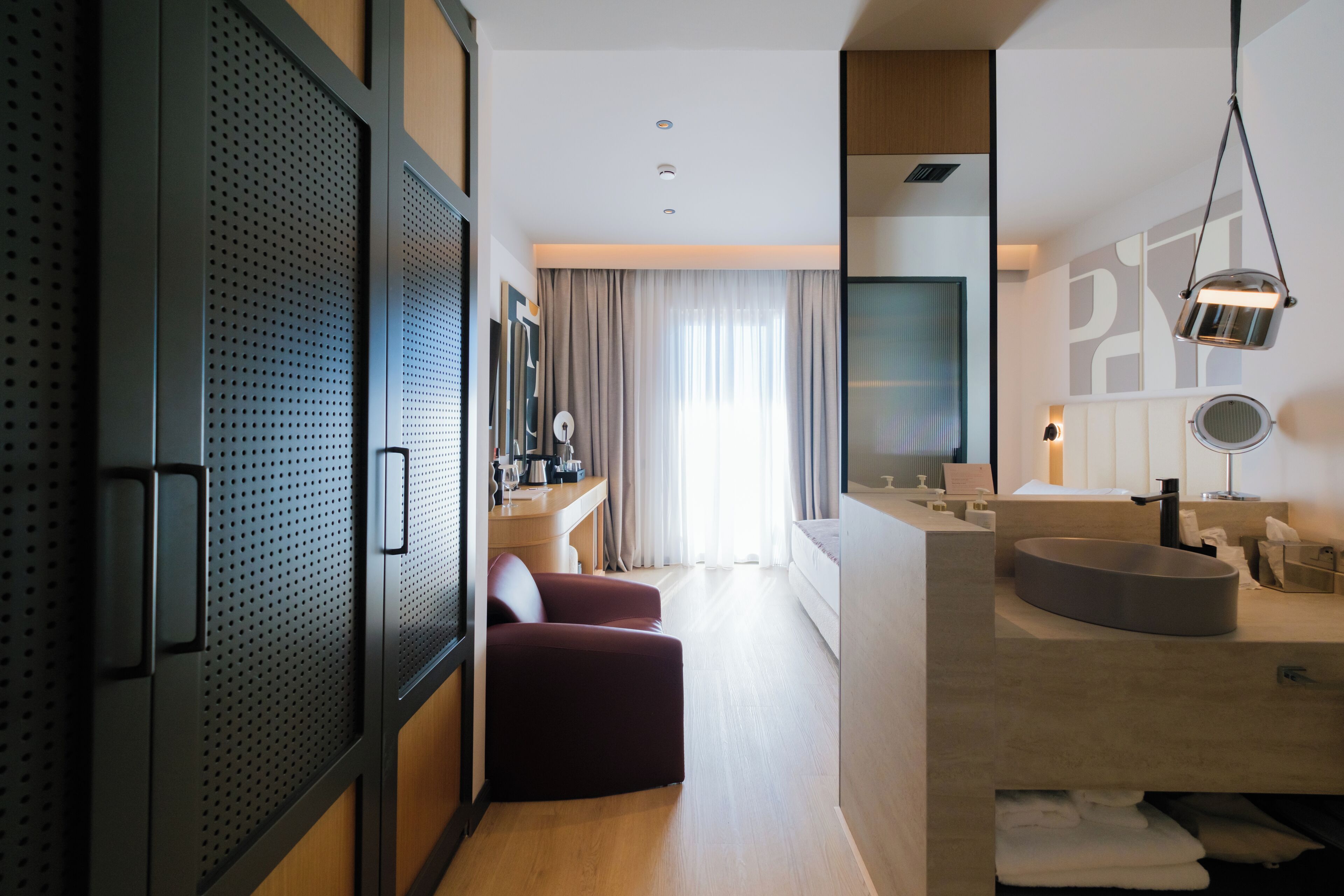 Ein modernes Hotelzimmer mit einem großen Bett, einem Schreibtisch mit Stuhl, einem runden Waschbecken und einem großen Spiegel.