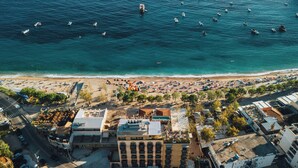An aerial view of a beach with numerous boats, a crowded beach area with umbrellas and people, and buildings with rooftop terraces. - Saint Nicolas (Himarë)
