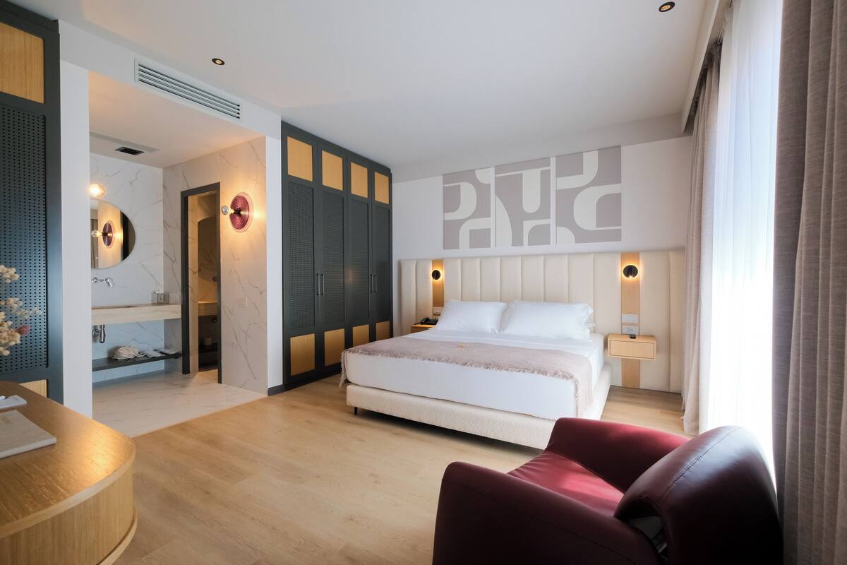 A modern hotel room with a large bed, a desk, and a vanity area.