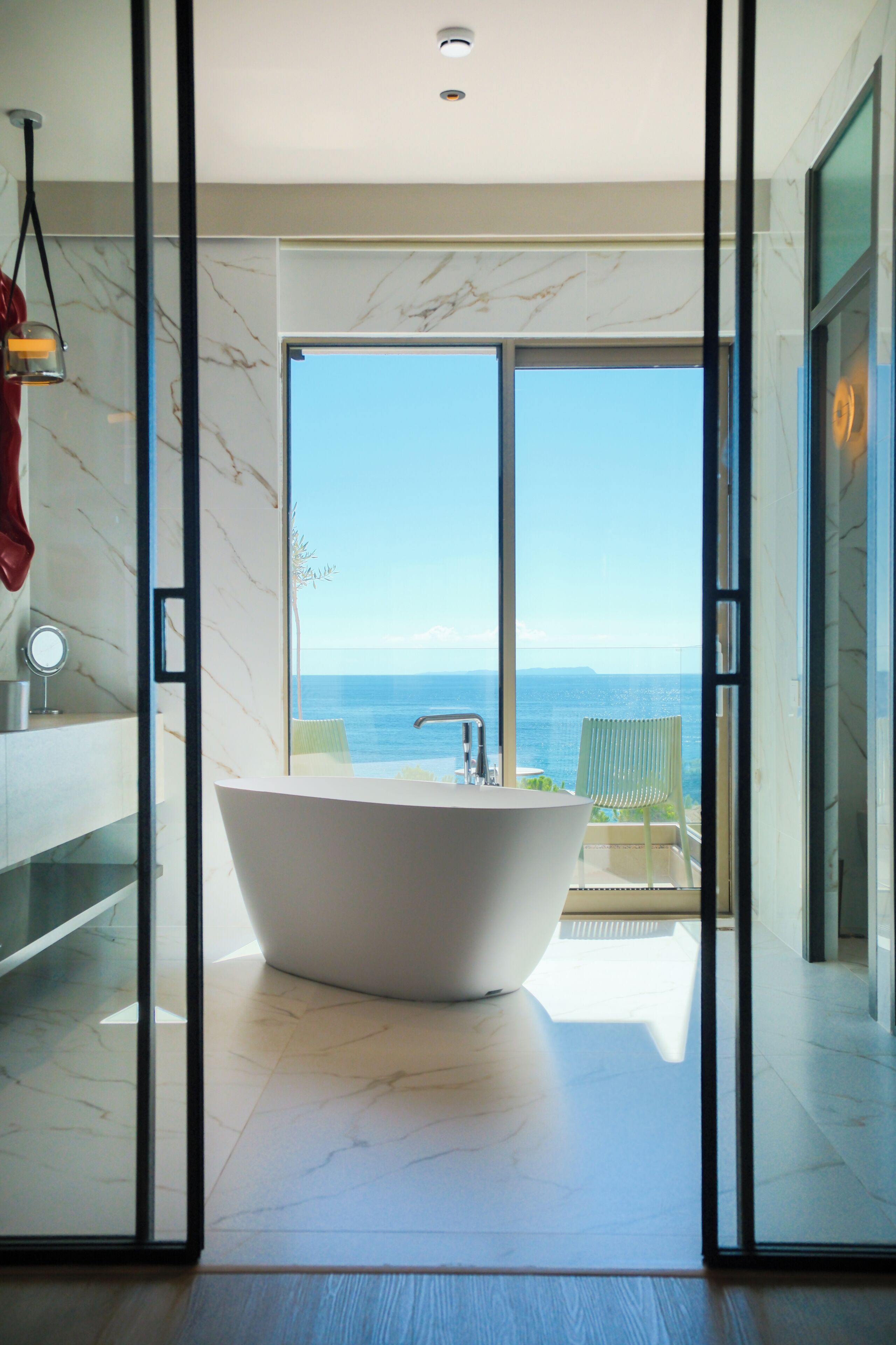 A modern bathroom with a freestanding bathtub, a glass shower enclosure, and a view of the sea.