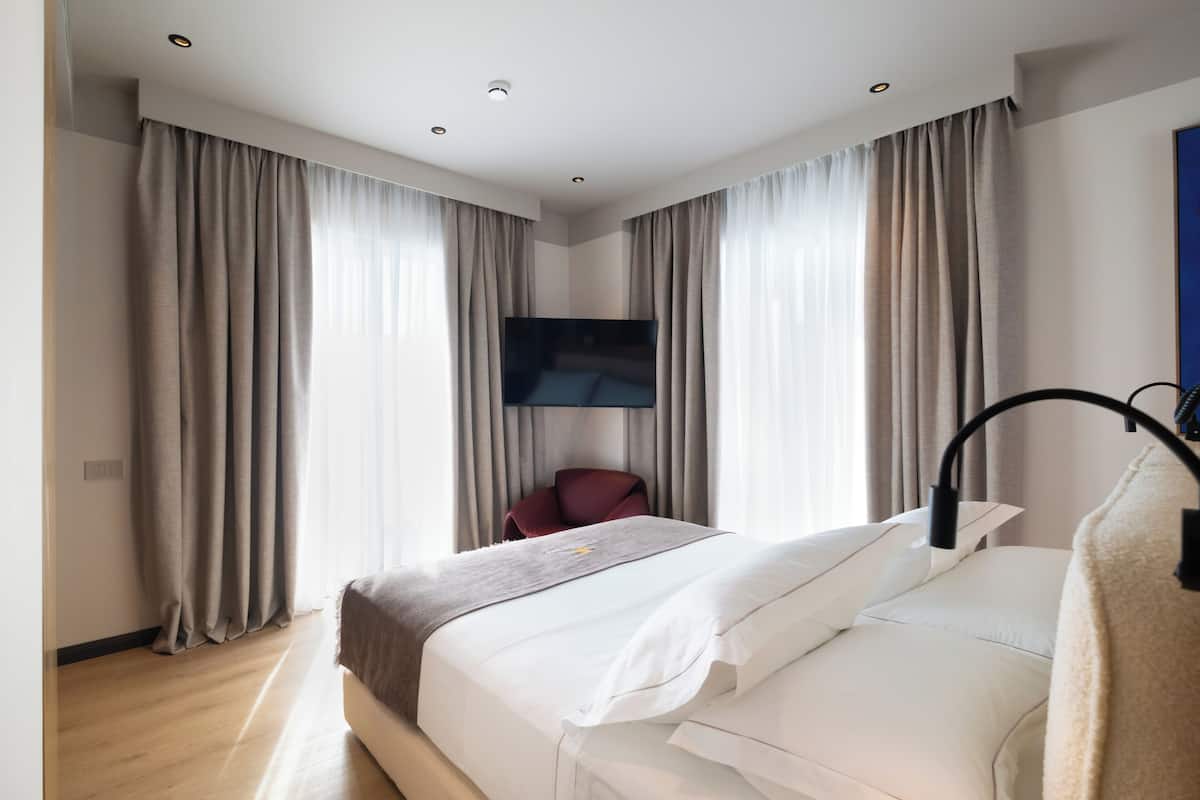 A modern hotel room with a large bed, a flat-screen TV mounted on the wall, and a red chair.