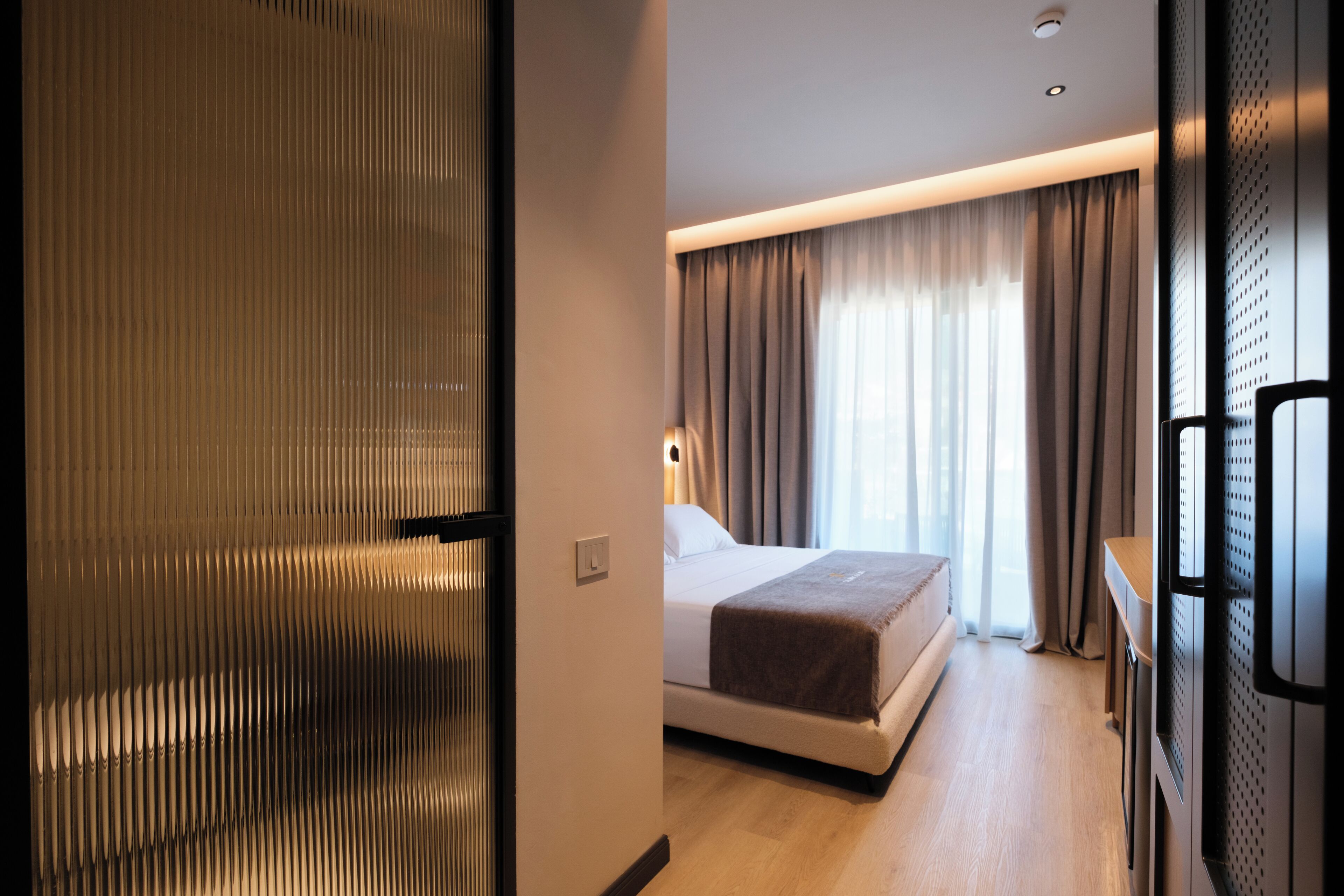 A hotel room with a bed, a desk, and a large window with curtains.