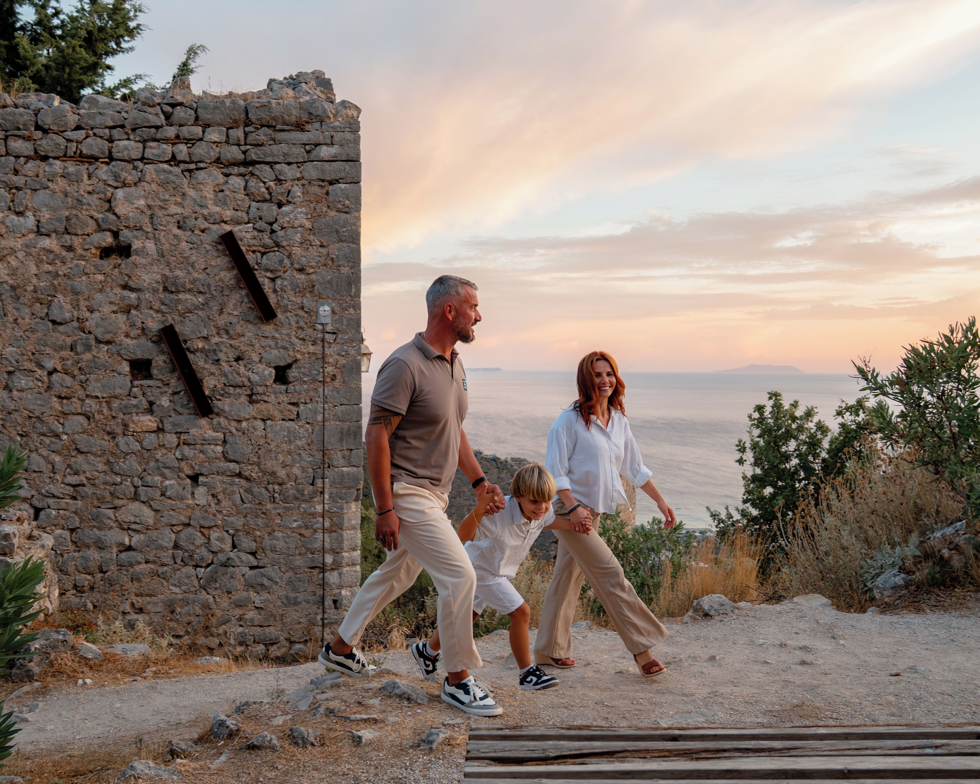 A family walking along a stone pathway with a view of the sea in the background.