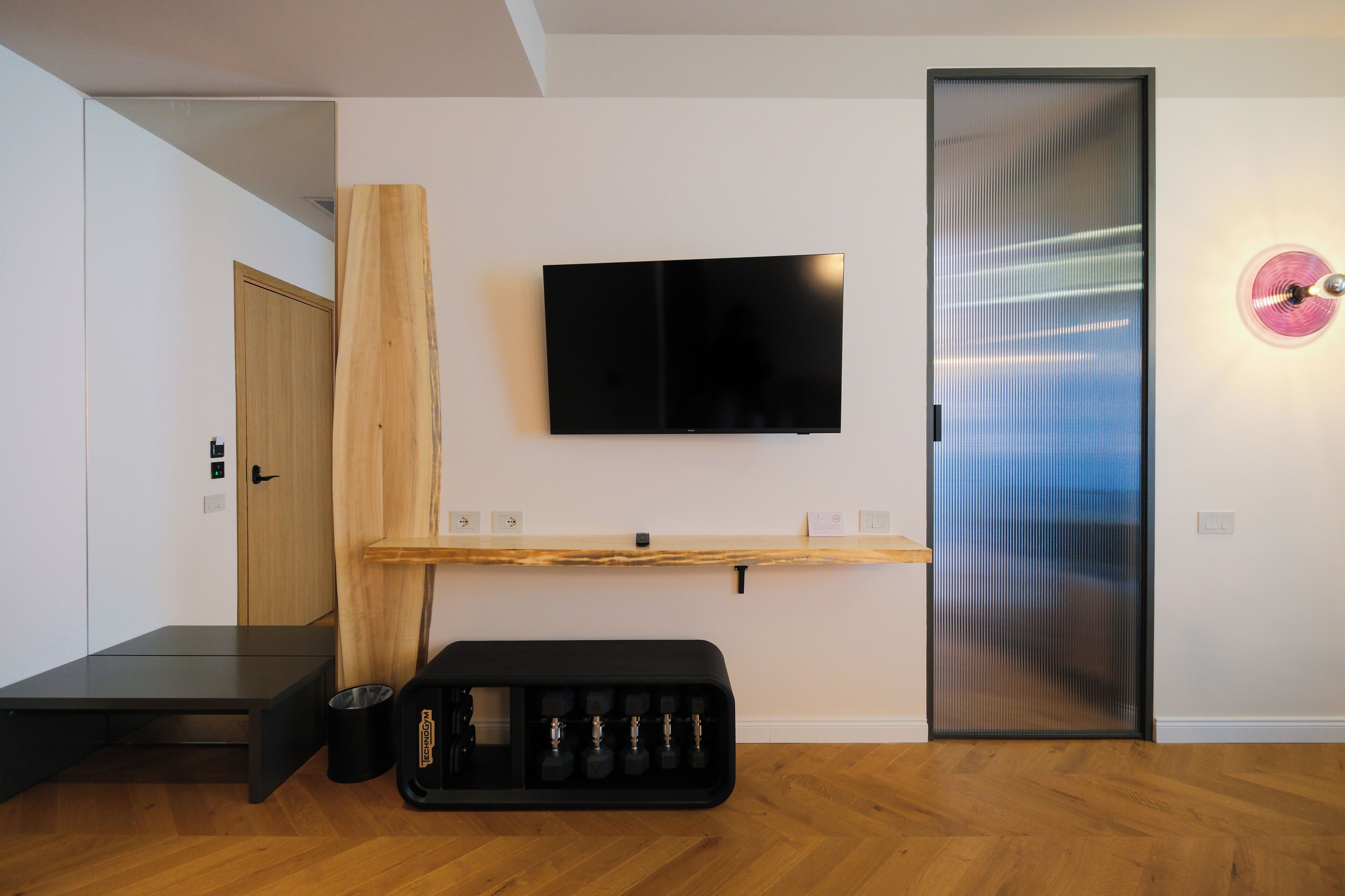 A modern room with a flat-screen TV mounted on the wall, a wooden door, a small shelf, and a black storage unit with multiple compartments.