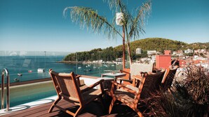 A deck with wicker chairs and a table overlooking a marina with boats and a hilly town in the background. - Saint Nicolas (Himarë)