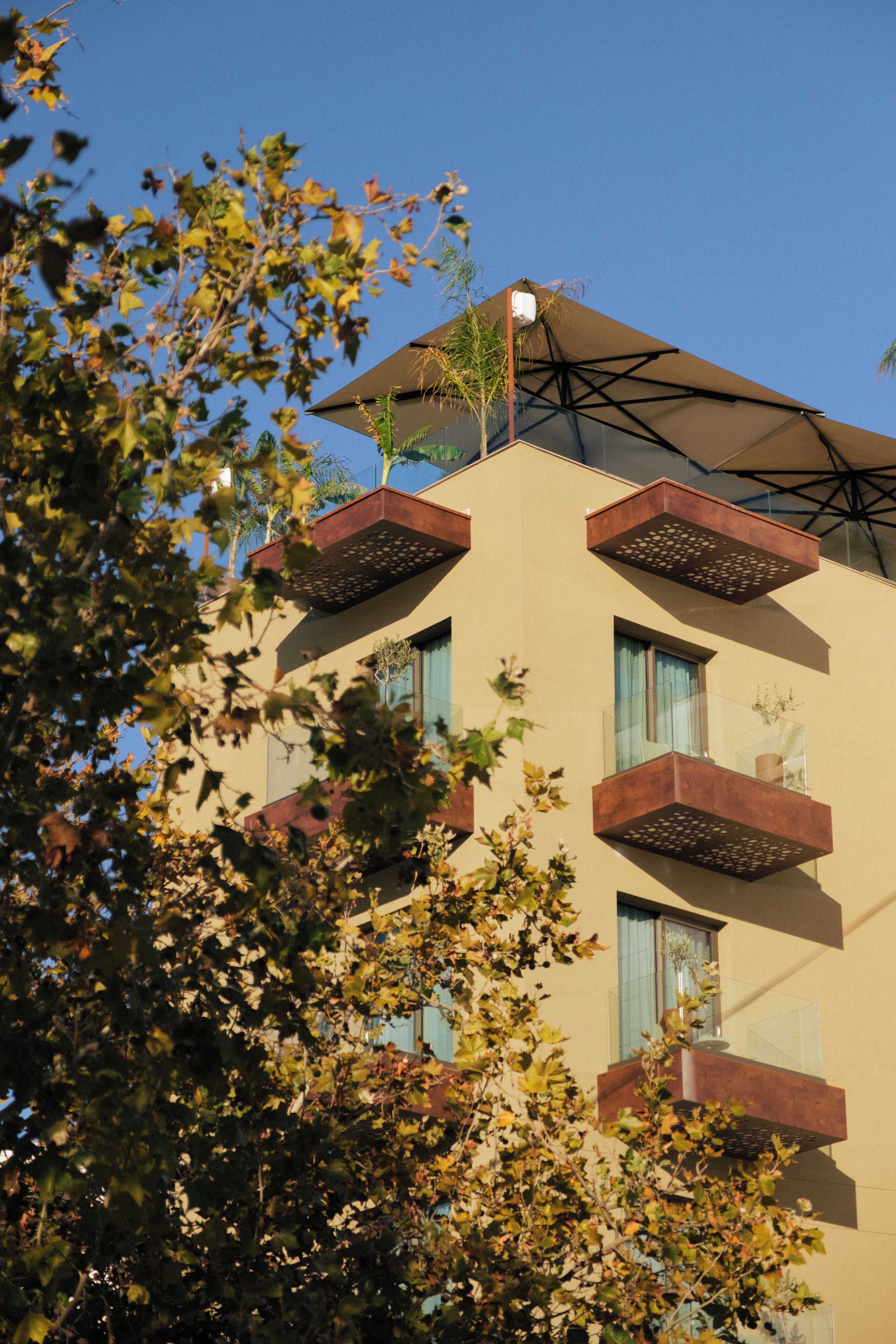 A multi-story building with balconies, a clear sky, and trees in the foreground.