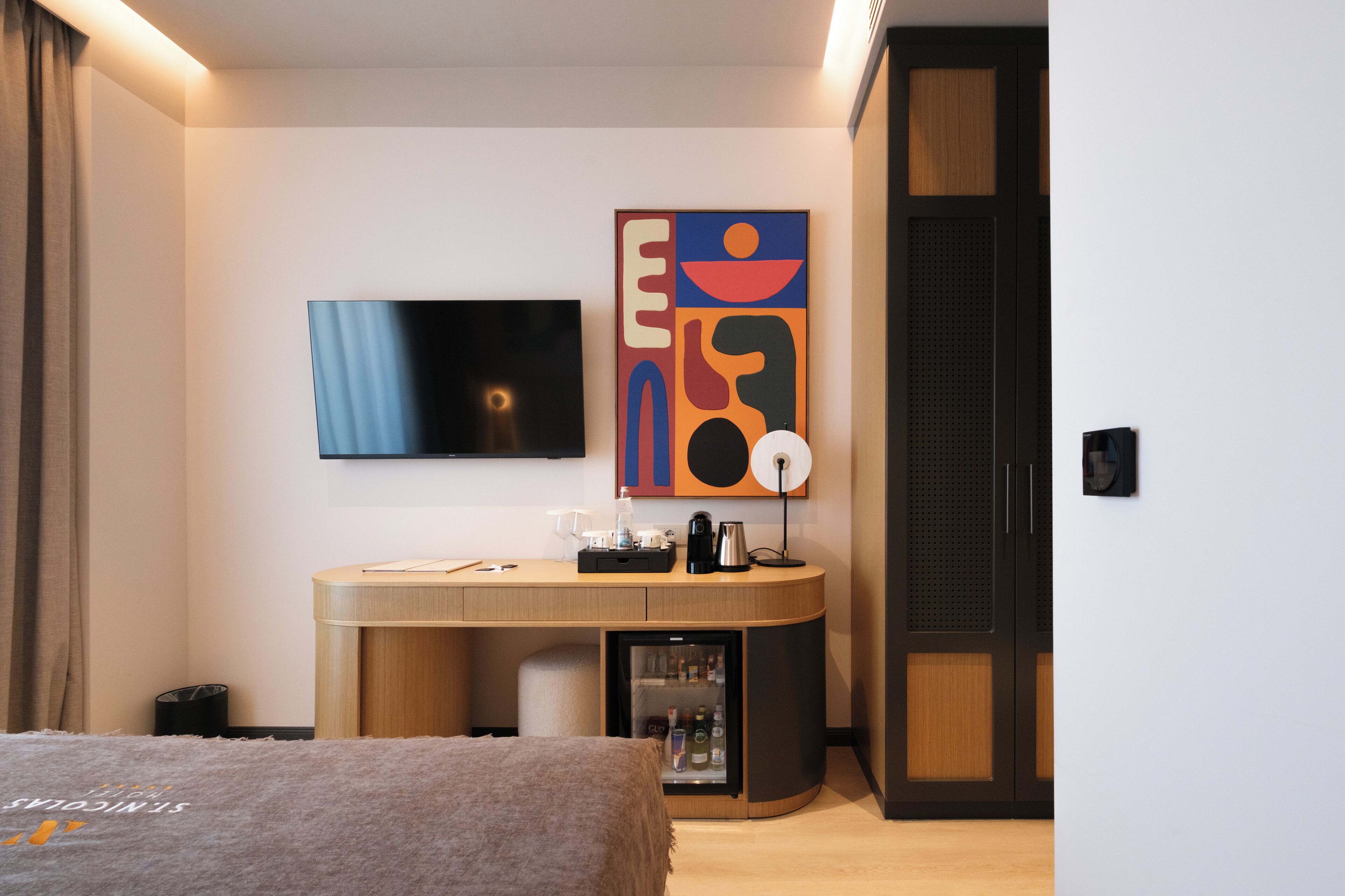 Una habitación de hotel moderna con cama, escritorio con cafetera, televisor y refrigerador.