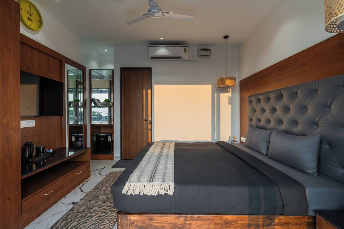 A bedroom with a large bed, a wardrobe, a television, and an air conditioning unit.