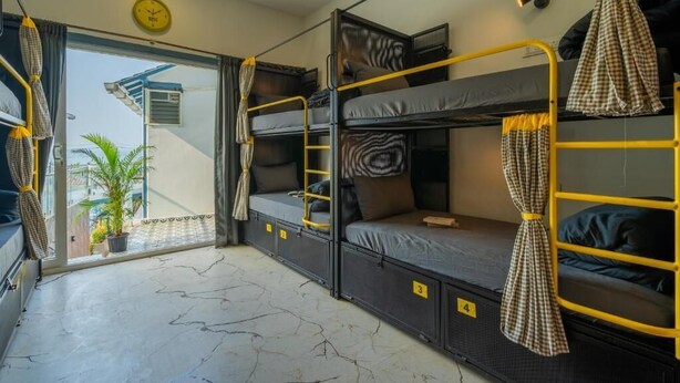 A dormitory room with bunk beds, a clock, and a view of the outside. - The Hosteller Goa, Mandrem (Mandrem)