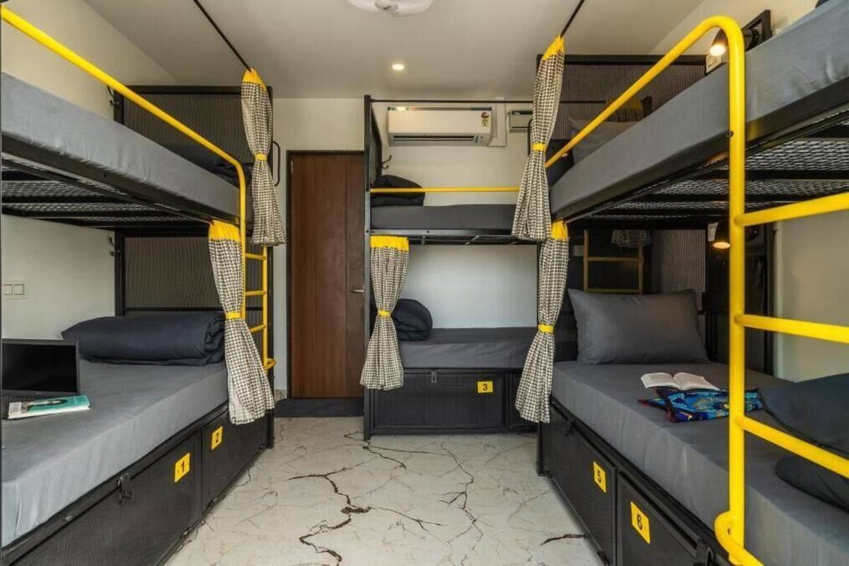 A dormitory room with bunk beds, a small desk, and a window.
