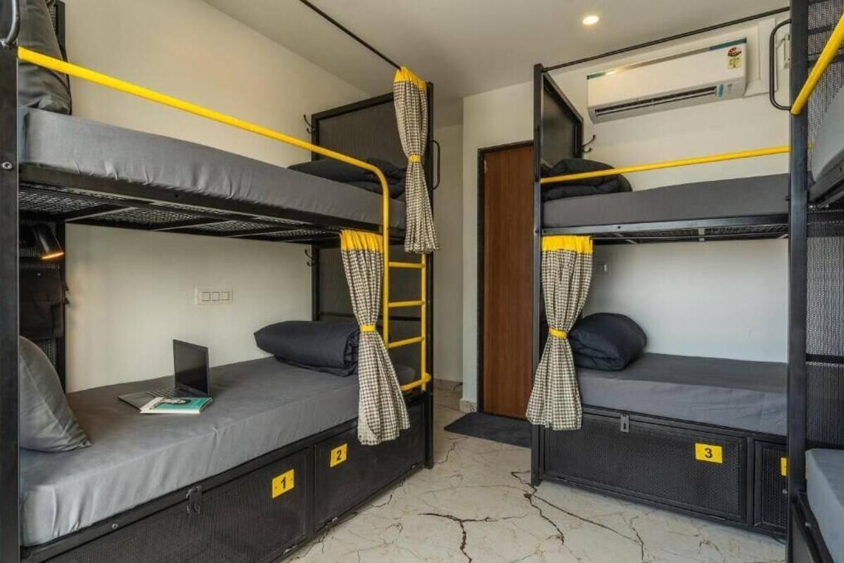 A dormitory room with bunk beds, a laptop on one bed, and a door with a number sign.