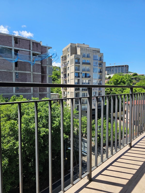 A balcony with a view of multi-story buildings, some under construction, and lush green trees.