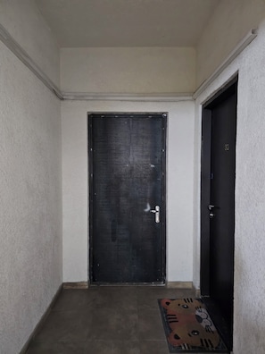 A hallway with a dark door, a smaller door with the number 31, and a patterned mat on the floor.