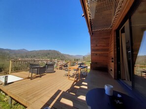 A wooden deck with outdoor furniture, a view of a village, and mountains in the background. - La maison en A, cosy and atypical chalet in the heart of the Ariège mountains (Seix)