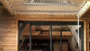 Een houten hutje met een schuifdeur die leidt naar een woonruimte met een bank, een salontafel en een potplant.