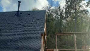 Een houten terras met een metalen glijbaan die naar een huis met donkere dakpannen leidt.