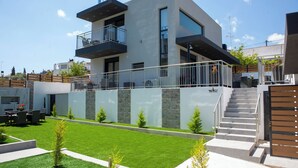 A modern two-story house with a balcony, a stone wall, and a well-maintained lawn. - Emma & Peris Villas-A Two Villa Retreat with Shared Courtyard,By IdealStay (Gouves)