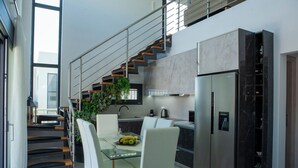 A modern kitchen with a built-in refrigerator, a dining area with a glass table, and a staircase with a railing. - Emma & Peris Villas-A Two Villa Retreat with Shared Courtyard,By IdealStay (Gouves)