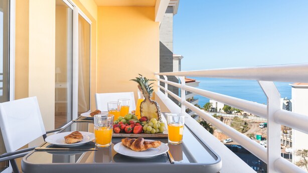 Un balcon avec une table préparée pour le petit-déjeuner, comprenant des croissants, des fruits et du jus d’orange.