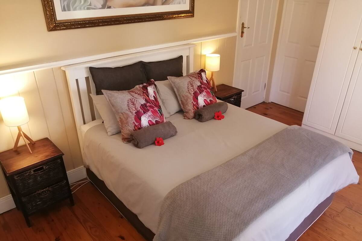A neatly made bed with a white headboard, two decorative pillows, a grey blanket, and a bedside lamp on a wooden nightstand.